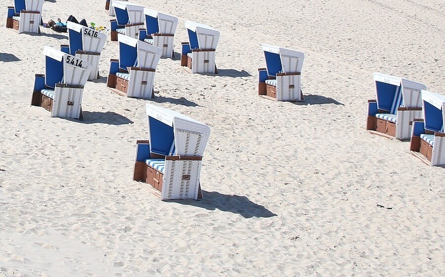Beach chairs on sand, with one chair and its long shadow in the foreground, before removal