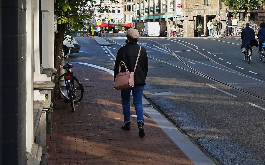 A pedestrian in a cap and coat walking away along a brick sidewalk beside a tram street, before removal